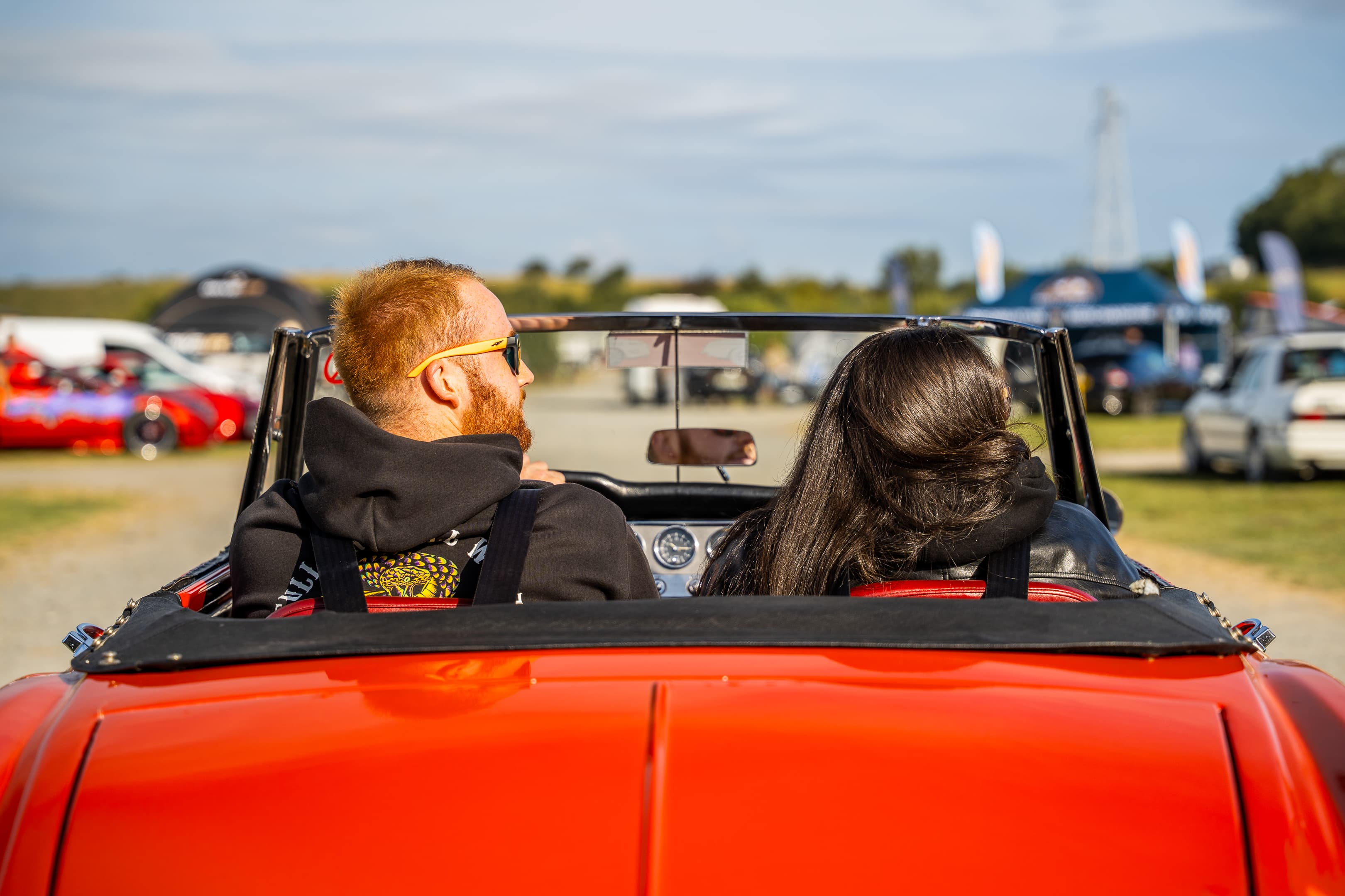 A couple riding in a red convertible classic car at The Weekender