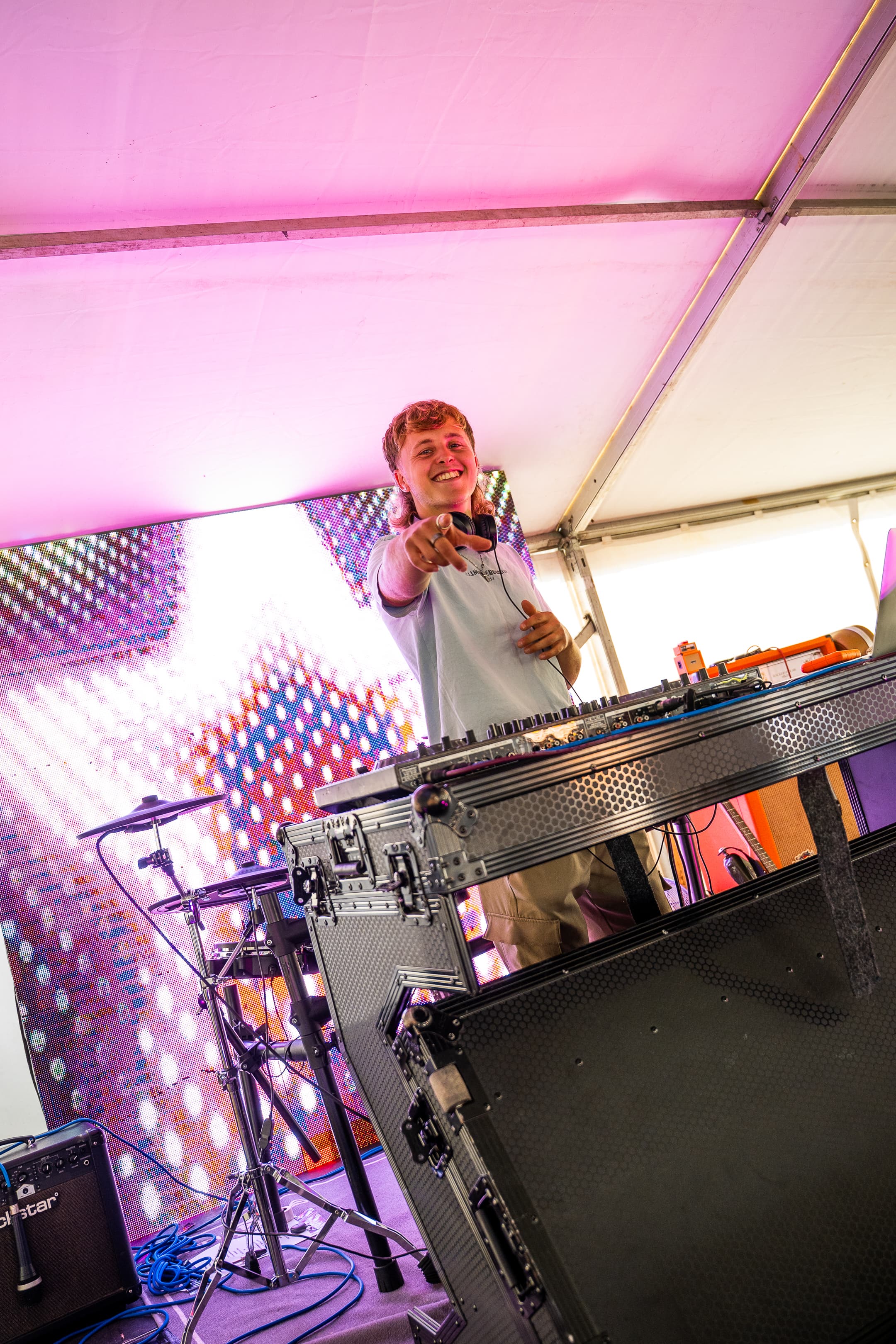A DJ performing under a marquee at The Weekender, with a colourful LED backdrop
