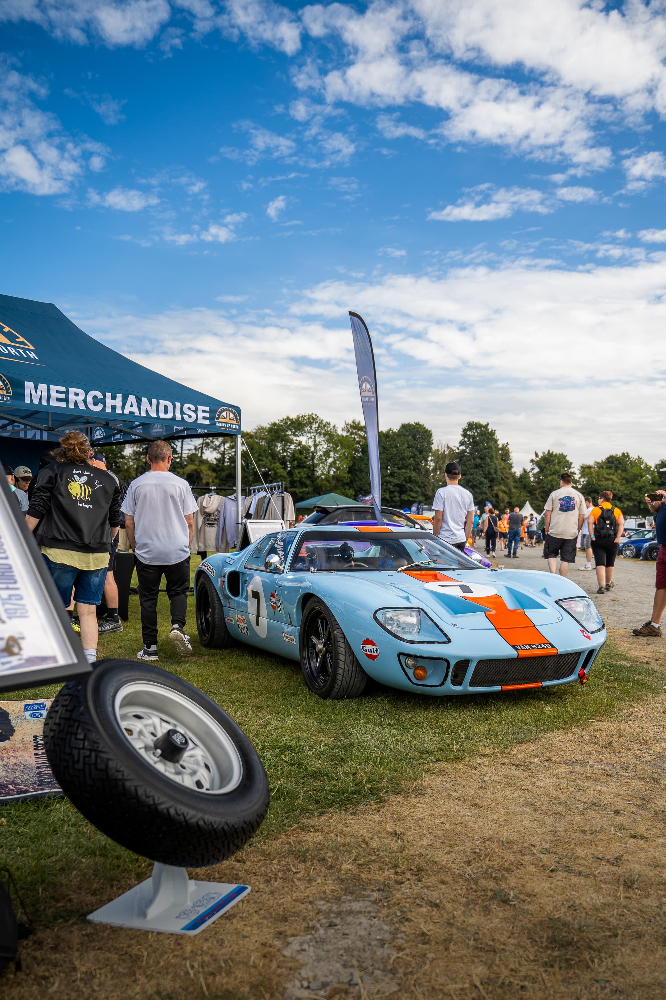 A blue and orange Gulf-liveried Ford GT40 parked near the WUN merchandise tent
